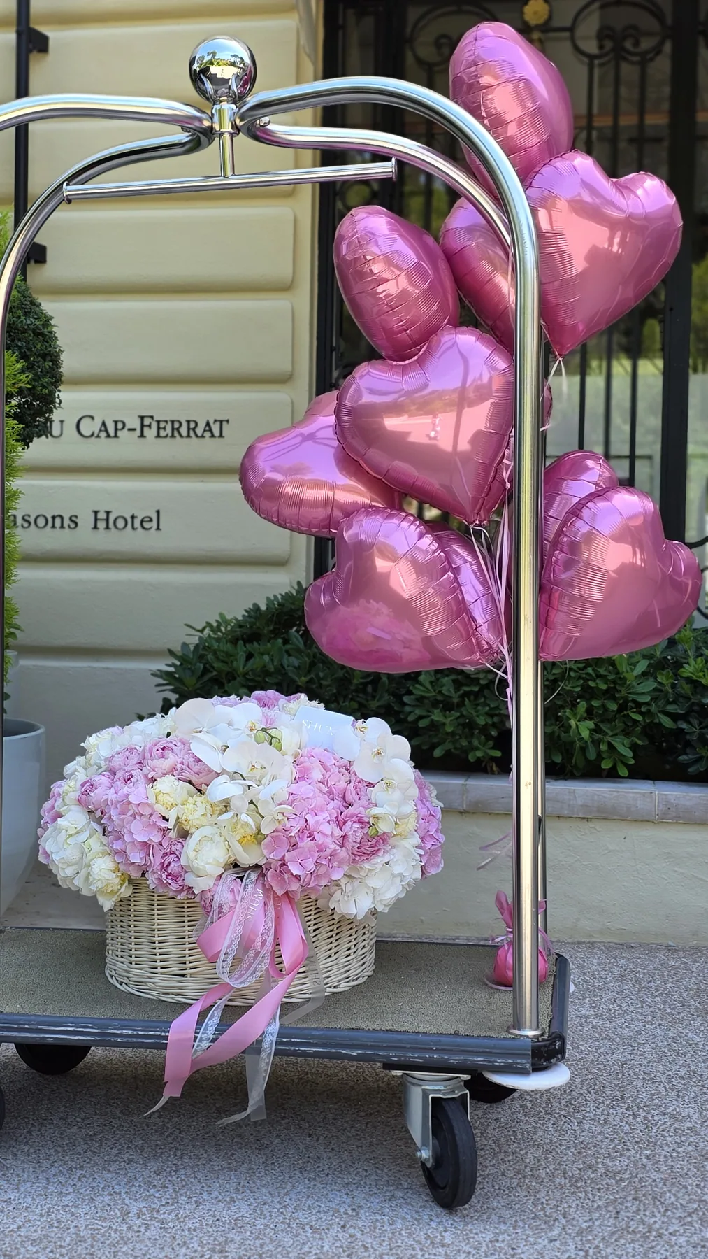 A basket of peonies and heart balloons at a hotel entrance